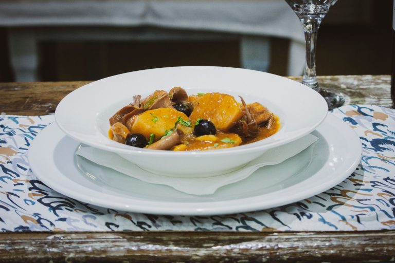 Delicious traditional Angolan stew featuring root vegetables and dark olives in a white bowl.