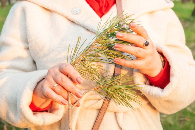 Close-up of a woman holding a pine branch wearing a warm coat in a natural setting.
